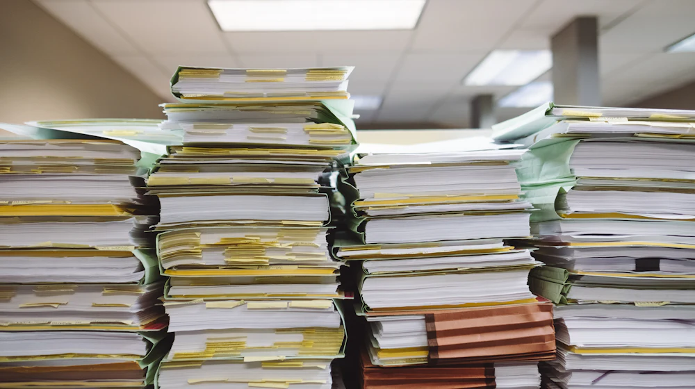 Stacks of paper personnel files and compliance documents in an office